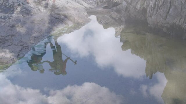 Caucasian senior couple hiking on rocks reflected in water, over fast moving clouds