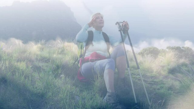 Happy caucasian senior woman resting while hiking in mountains, over fast moving clouds