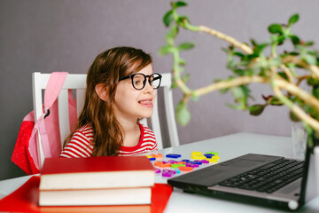 Happy girl kid 6-7 y.o. uses a laptop to study at home with a teacher, a speech therapist. Distance learning.