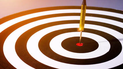 Smart goal concept, Gold dart arrow hitting in the target center of dartboard on bullseye with sun...