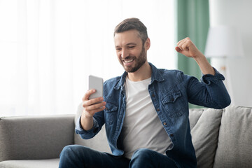 Emotional bearded man celebrating success, using mobile phone