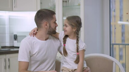Joyful beautiful little girl and happy young man kissing and laughing resting at home on weekend. Portrait of cheerful Caucasian father and daughter enjoying time together indoors