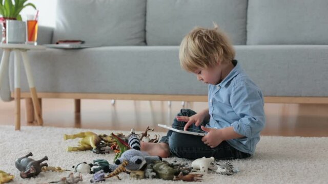 Cute blond child, toddler boy, playing at home with dinosaurs, sitting on the floor