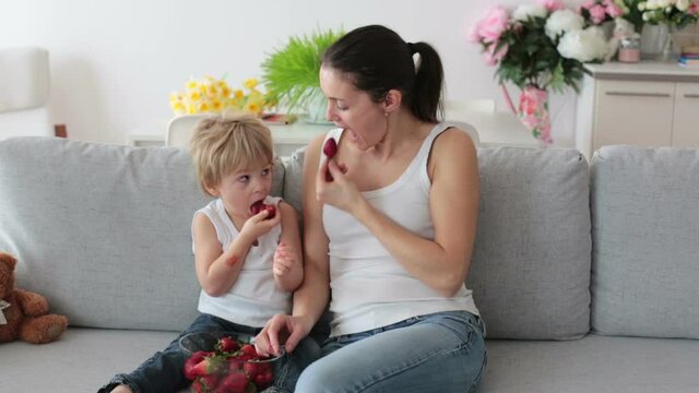 Mother and child, eating strawberries and having fun at home, sitting on the couch
