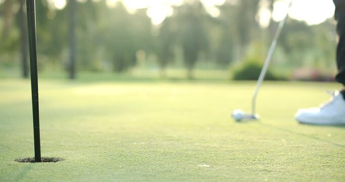 Close up shot of golf ball rolling into the hole. Golf player putting a golf ball into hole in slow motion.