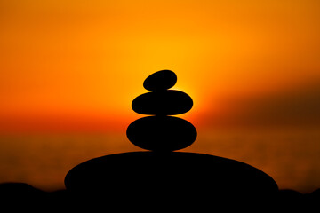 Rock pebble pyramid silhouette at sunset, zen stones on sea beach, meditation, spa, harmony, calm background, balance concept