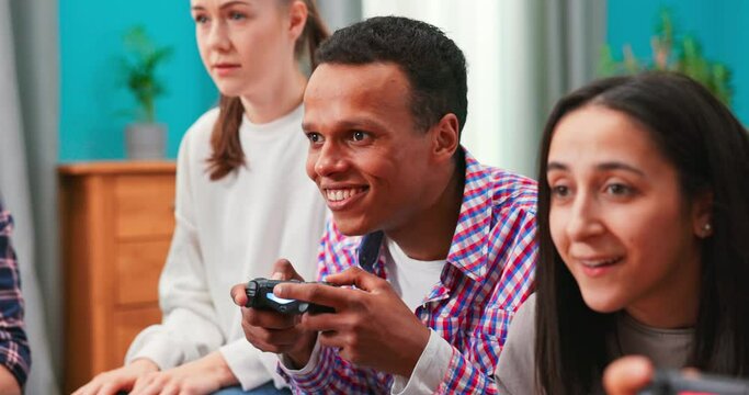 Black African-American excited man sitting on a sofa, holding a joystick playing video games, feeling overjoyed in addicting game alone at home, using video game console