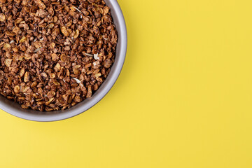 Organic homemade roasted granola cereal with oats, flax, almonds, chocolate in round baking tray on bright yellow background. Top view, flat lay muesli with copy space