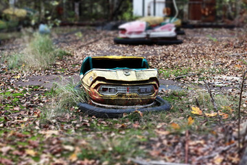 Old broken abandoned rusty metal radioactive yellow car among moss and autumn leaves in amusement park in ghost town Pripyat, Chernobyl Exclusion Zone. Tilt-shift effect