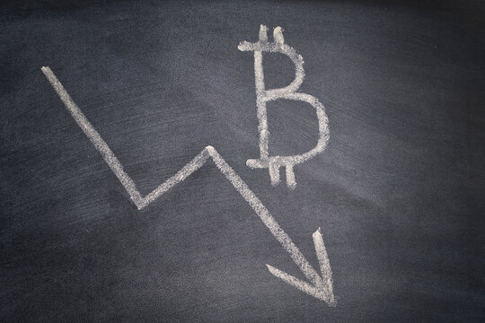 the price of the bitcoin is going down. the simbol of cripto written on a blackboard and an arrow down