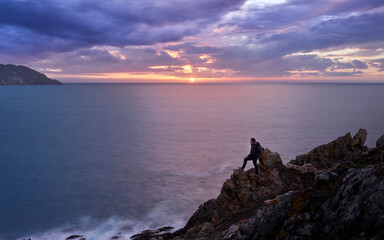 Silhouette of a man on the rocks of a cliff watching an imposing sunset in the ocean with C&iacute;es Islands in the background at Cabo Home, Galicia   
