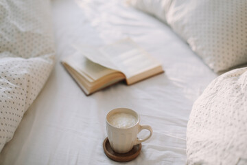 Fototapeta na wymiar Open book on bedsheets and a cup of coffee. Good morning. Breakfast in bed. flat lay