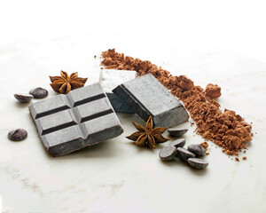 Dark chocolate bar, chocolate chip and powder cocoa on a marble table, besides some anise stars.