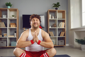Peaceful thick funny guy in sportswear doing meditation folding hands in pray gesture relaxing in...