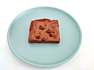 Homemade chocolate chip brownie served in soft teal plate isolate on white background. Selective focus.