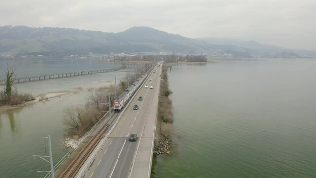 Aerial following cars and a train driving over the Seedamm, dam in Rapperswil.