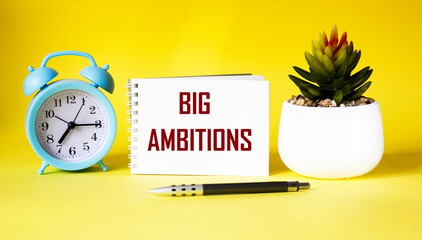 text BIG AMBITIONS on notepad and yellow background.