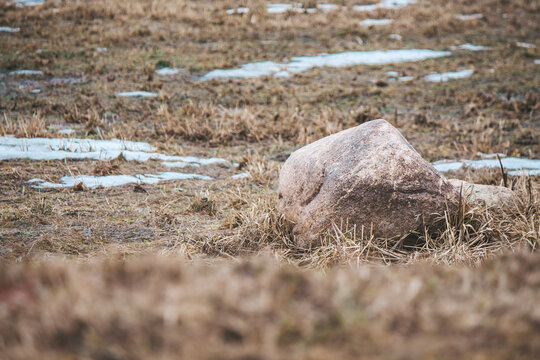 A large stone lies on muddy ground between patches of snow