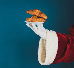 Hand of Santa Claus with croissants on a dark turquoise background with copy space.