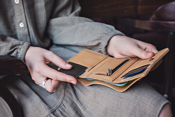 The woman holds an open wallet in her hands to take out a credit card and pay the bill at the cafe. Close-up, no face, copy space, horizontal orientation.