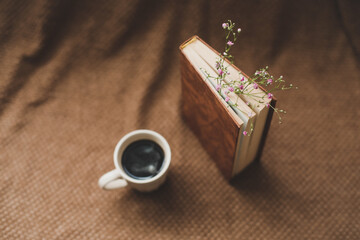 A book with flowers and cup of coffee on dark background top view