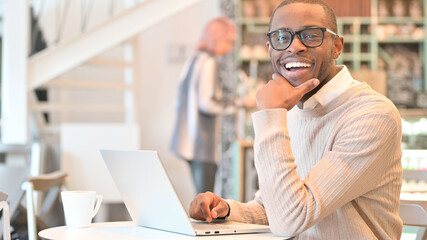 Cheerful Man with Laptop Smiling at Camera in Cafe 