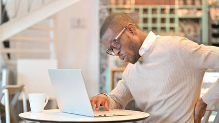 Fototapeta na wymiar Hardworking African Man with Laptop having Back Pain in Cafe