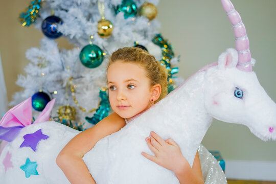 Emotional beautiful young girl in Christmas decorations background with big unicorn stuffed toy. New year concept.