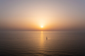 Naklejka na ściany i meble Sail boat sailing slowly towards a setting Sun in the Mediterranean Sea.