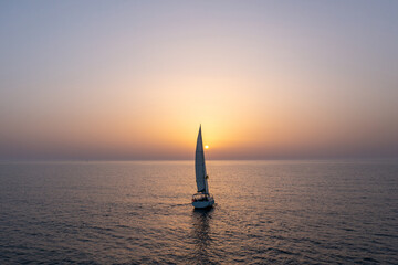 Sail boat sailing slowly towards a setting Sun in the Mediterranean Sea.