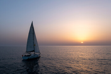 Sail boat sailing slowly towards a setting Sun in the Mediterranean Sea.