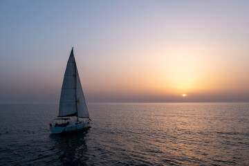 Fototapeta premium Sail boat sailing slowly towards a setting Sun in the Mediterranean Sea.