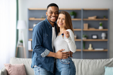 Happy young multiracial couple holding home keys and hugging