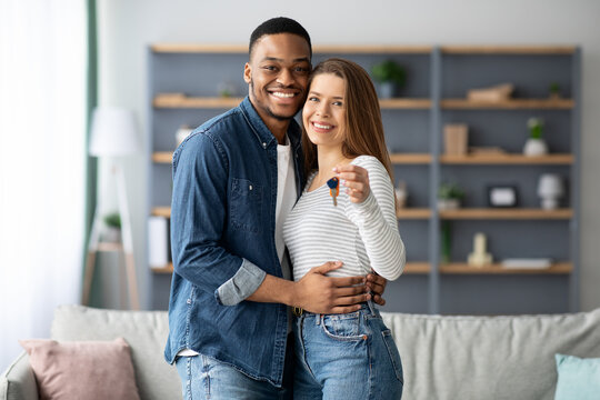 Happy young multiracial couple holding home keys and hugging