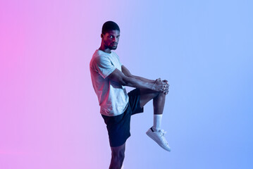 Portrait of athletic black man stretching his leg in neon lighting. Healthy lifestyle concept