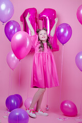 beautiful girl with pink make up and in pink leather dress. near colorful balloons in shape of number eleven 11. on pink background. concept of birthday party celebration.