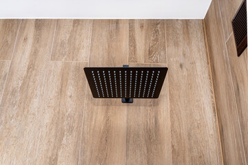 A modern, black metal concealed shower with a large rain shower, placed on tiles.