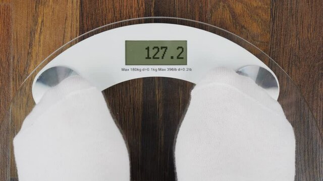 Overweight on bathroom scales digital display. Concept of tackling overweight and obesity. A person steps on weight scales to check her weight. Close-up, first-person view