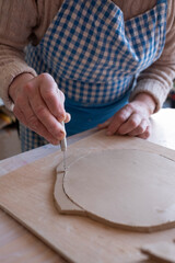 Senior female artist cutting wet clay creating a plate