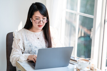 Happy of asian freelance people Businesswoman wearing wireless earphones casual working with laptop computer with a coffee cup mug,Notebook and smartphone at the cafe,Business Lifestyle communication