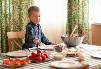 Little blond boy at a feast, choosing food. A festively laid table, Christmas, New Year, Birthday Eve