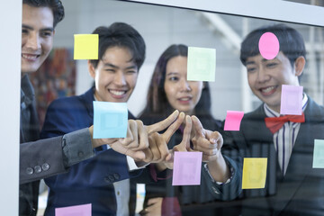Fototapeta na wymiar Successful happy workers Group of asian business people with diverse genders (LGBT) and use post it notes to share idea. Brainstorming concept. Sticky note on glass wall in the meeting room at office