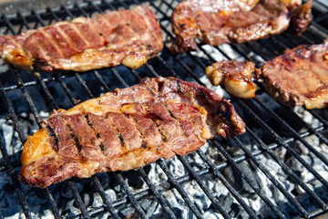 Fresh beef steaks being fried or prepared on grill or BBQ with pepper, spices and seasoning, delicious food.	