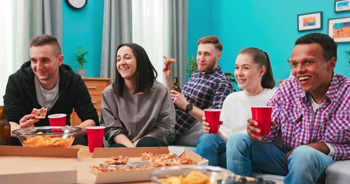 Cheerful friends enjoying pizza together at home. Happy smiling men and young women sharing pizza for dinner. Group of multiethnic guys and girls having party and eating sitting around the table.
