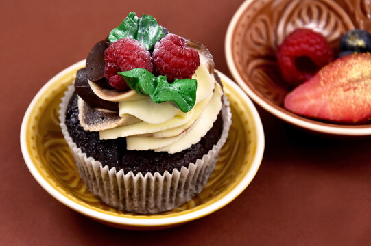 Chocolate vanilla cupcake with raspberries still life stock images. Delicious creamy cupcake with berries on a brown background stock photo. Fresh cupcake with berries close-up stock images