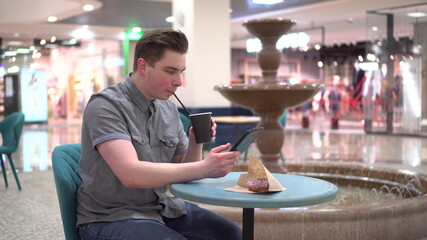 A young man in a cafe with a tablet in his hands against the background of a fountain. Decoration in the cafe.