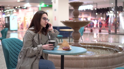 A young woman in a cafe speaks on the phone against the background of a fountain. Decoration in the cafe.