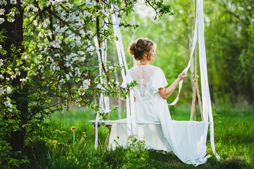 Young bride with blond hair in white negligee posing on a rope swing