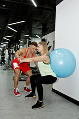 Obraz na płótnie Canvas the trainer explains to the newcomer girl how to exercise on the in the gym. A pumped-up teacher helps a thin woman athlete to rehabilitate and achieve success. Training with a personal trainer