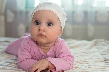 A child in pink clothes and a hat lies on the bed